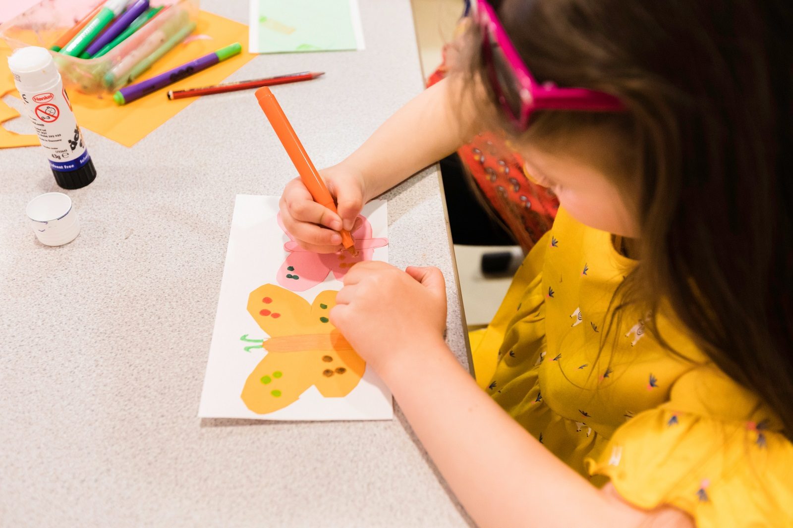 A young girl decorstes a piece of paper with a yellow butterfly design