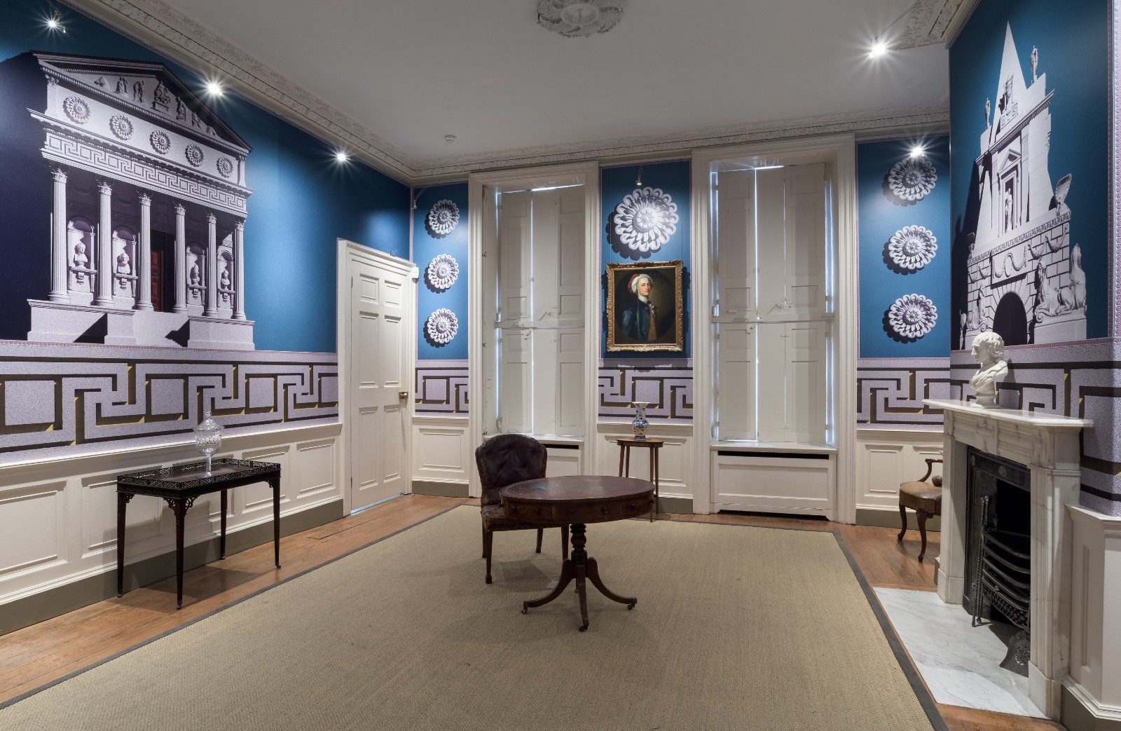 The interior of a period house with wallpaper decorated with outsized classical buildings and architectural features against an electric blue background.